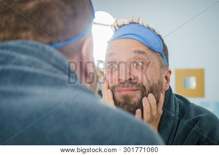 Adult Man With Eyemask On His Forehead Feeling Fresh After Waking Up, Looking At Himself In Bathroom