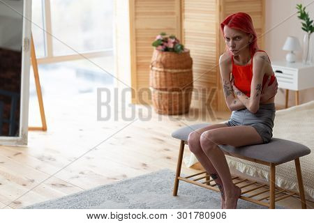 Red-haired Anorexic Woman Sitting In Bedroom Near The Window