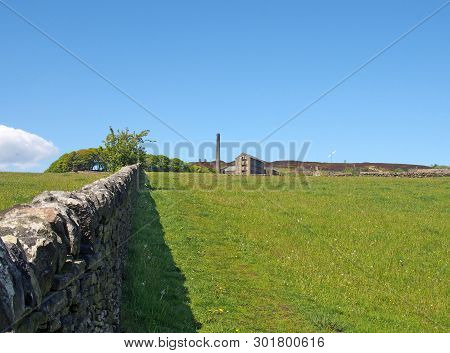 A Long Stone Wall In Perspective Bordering A Green Grass Meadow In Bright Spring Sunlight With A His
