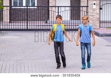 Two Happy Shoolboys With Backpacks Go To School In The Morning.