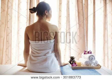 Young Woman Spending Day In Spa Salon. She Is Sitting Next To Tray With Towels And Essential Oils
