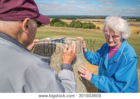 Elderly Couple At The Trig Point,danebury Ring, In The British Countryside.