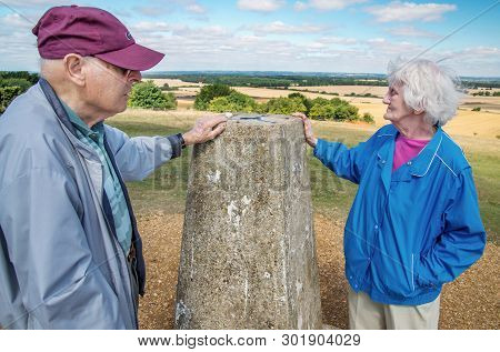 Elderly Couple At The Trig Point,danebury Ring,wiltshire, In The British Countryside.