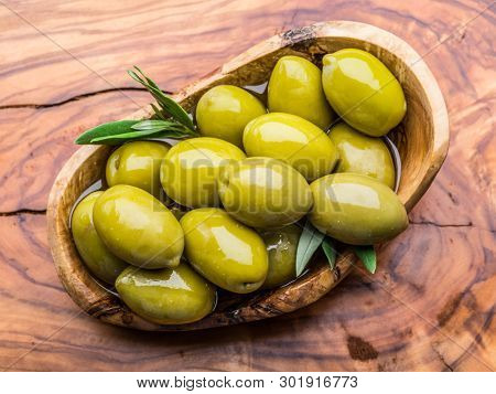 Whole table olives in the wooden bowl on the table. Top view.