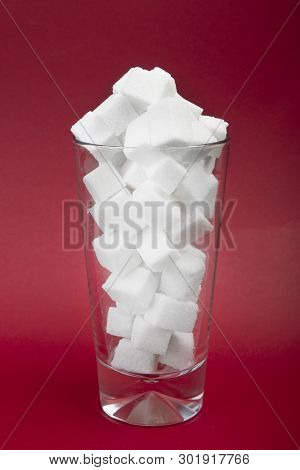Danger Of Sugar In Carbonated Drinks. Concept Of Obesity. White Sugar Cubes On The Glass On Red Back