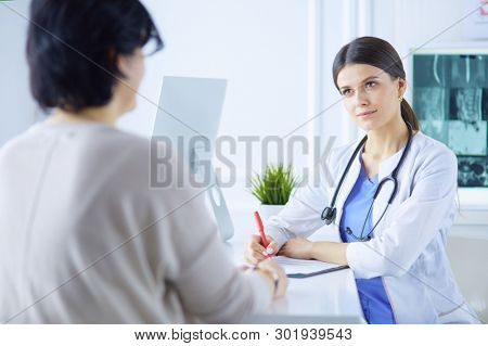Doctor and patient discussing medical problems in a hospital consulting room. Doc filling in a patient's form
