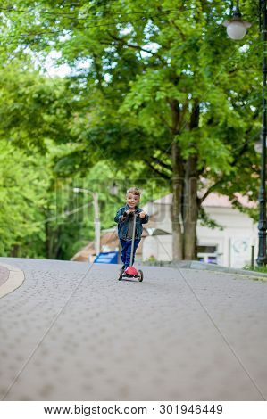 Little Boy Riding Scooter In City Park In Aummer. Kids Sports Outdoors. Happy Child Playing With His