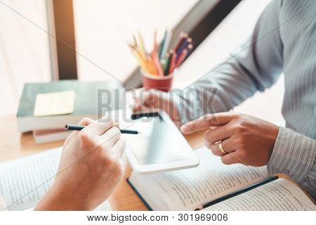 High School Or College Students Studying And Reading Using Tablet Together In Library