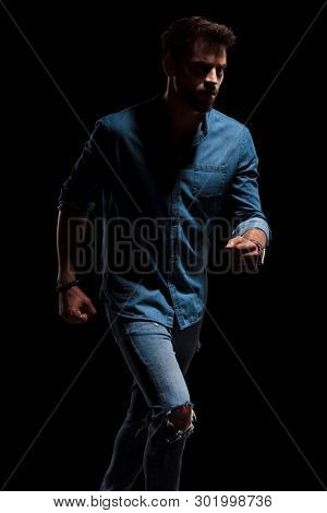 Brave man running to the side while wearing a blue shirt and jeans with a light shade hitting him on black studio background
