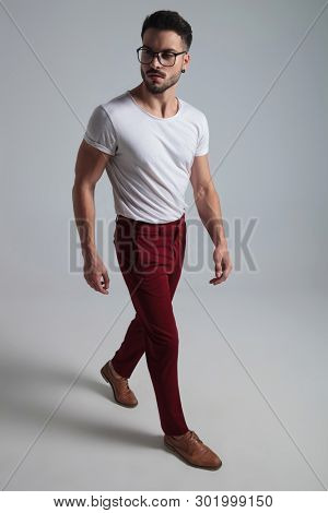 Confident young man stepping and looking sideways while wearing a white t-shirt and red pants on gray studio background