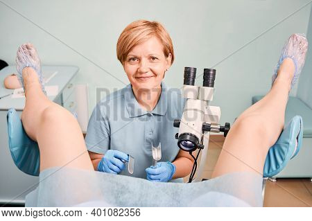 Female Doctor In Sterile Gloves Using Colposcope And Gynecological Retractors While Examining Woman 