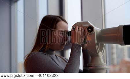 Young Woman Looking Through Stationary Binoculars. Media. Side View Of A Young Girl At The Observati