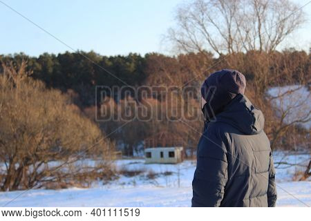 The Man Stands With His Back To The Camera And Looks Into The Distance Against The Background Of A S