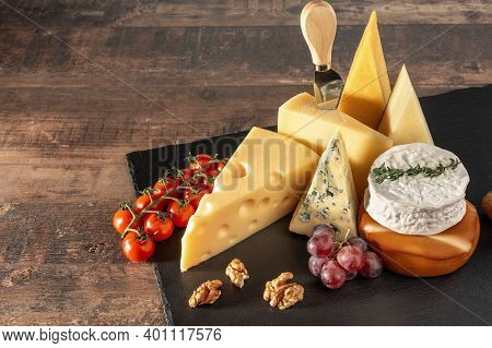 Collection Of Swiss, French, Italian And Holland Cheeses On A Black Cheese Board Served With Fruit, 