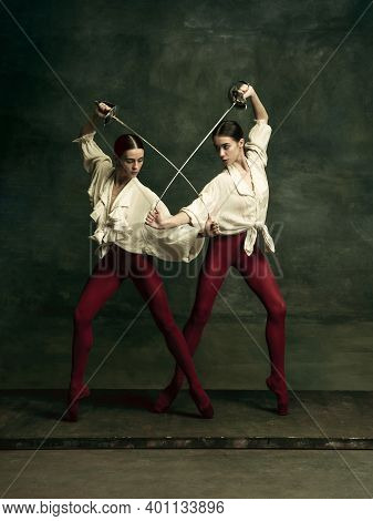 Contrast. Two Young Female Ballet Dancers Like Duelists With Swords On Dark Green Background. Caucas