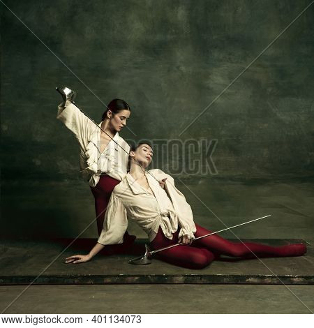 Tragic. Two Young Female Ballet Dancers Like Duelists With Swords On Dark Green Background. Caucasia