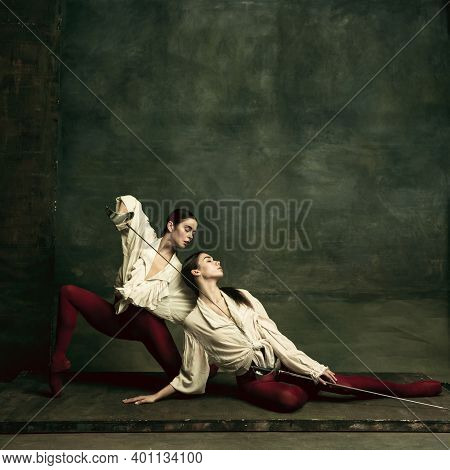 Tragic. Two Young Female Ballet Dancers Like Duelists With Swords On Dark Green Background. Caucasia