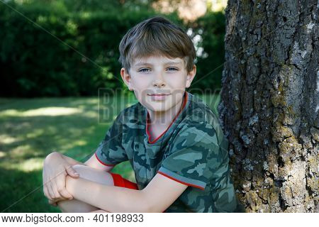 Outdoor Portrait Of Happy Smiling Preteen Kid Boy On Sunny Summer Day In Park Near Tree. Handsome He