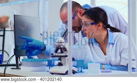 Chemist Nurse Explainig To Doctor Vaccine Development In Modern Equipped Laboratory Pointing On Comp