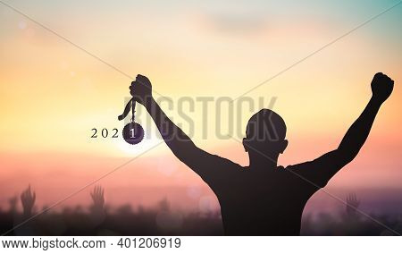 Success New Year 2021 Concept: Silhouette Winner Hand Holding Gold Medal Reward With Text For 2021 A