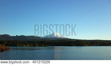 Nature of Chile, Beautiful panoramic landscape, lake Villarrica and snow capped Villarrica volcano under blue sky evning light. Pucon