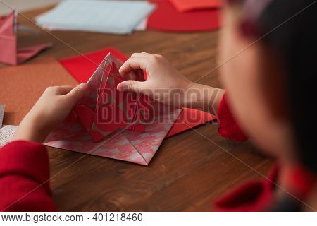 Unrecognizable Little Asian Girl Sitting At Wooden Table Making Origami Crane Using Colored Paper, O
