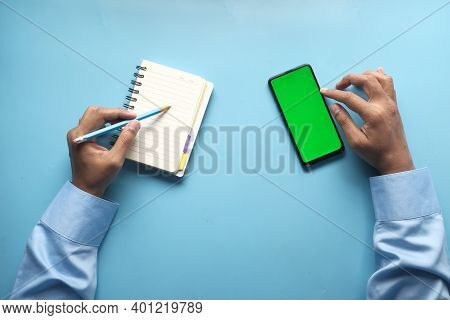 Top View Of Man Hand Using Smart Phone And Writing On Notepad