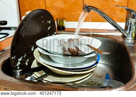 Dirty Dishes In The Kitchen Sink, Flowing Tapwater, Focus On The Wood Knife Handle.