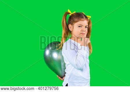 Serious School Girl Hides A Ultimate Gray Balloon Behind Her Back. Green Background And Side Space.