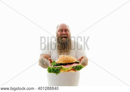 Isolated Portrait Of An Overweigh Man With Tattooed Arms Holding A Big Burger With Lettuce Leaves An
