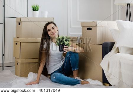 Young Woman With A Home Plant Sitting On The Floor In The New L