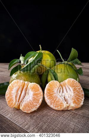 Fresh green tangerine mandarin orange with fresh leaves on dark wooden table background harvest concept.
