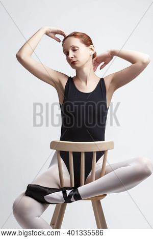 Ballet Concepts. Caucasian Female Ballet Dancer In Body Suit And Pointes Shoes Sitting On Chair With