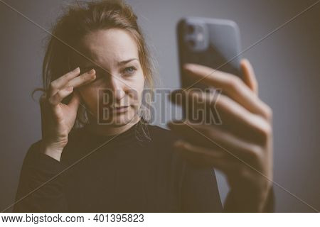 Young woman holding a phone, tired and exhausted, blue light straining her eyes, messing up her circadian rhytm