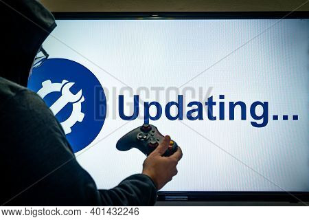 Hooded Man Holding A Gaming Controller In Front Of A Screen Showing An Updating Message For A Game O