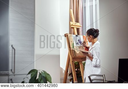 Side View Of A Woman Painter With Gathered Hair In A Bun And Paint Brushes In Her Hair Standing In F