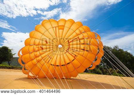 A Bright Orange Parachute Lies On The Sand Near The Water To Attract People To Fly And Look At The S