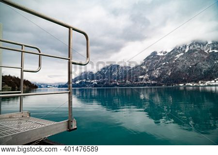 Peir On Swiss Lake With Metal Dock And Railing Mountain Peaks And Blue Water Of Lake Brienz