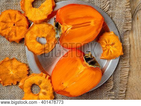 Ripe Delicious Orange Persimmons And Dried Persimmons, Top View. Fresh Halves Of Persimmon On A Meta