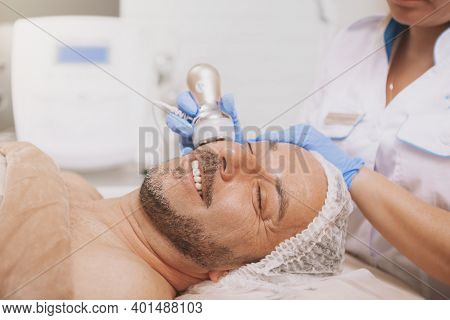 Relaxed Handsome Mature Man Smiling, Getting Ultrasound Cavitation Treatment By Professional Cosmeto