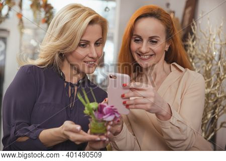 Cheerful Red Haired Mature Woman Enjoying Shopping At Home Decor Store With Her Friend, Using Smart 