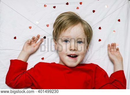 A Kid Todder Child Lies On A Bed With Hearts. Concept Of First Love And Valentines In Kindergarten A