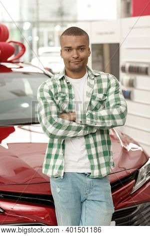 Vertical Shot Of A Young Handsome African Man Posing Proudly In Front Of His New Automobile At The D