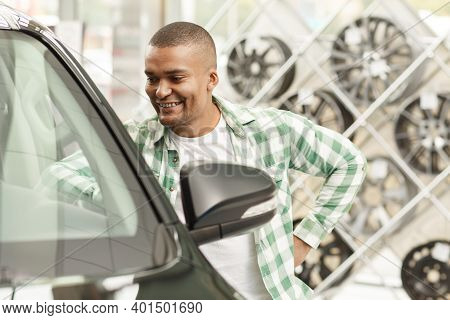 Young Happy African Man Posing Near His New Automobile At The Dealership Showroom. Cheerful Male Dri