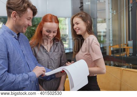 Cheerful Office Workers Laughing, Discussing Papers On Clipboard