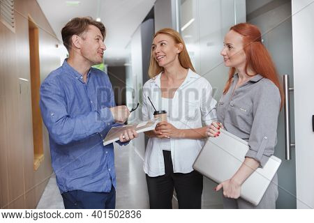 Cheerful Office Workers Talking In The Corridor While Having Coffee Break