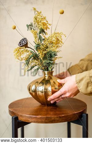 Female Decoarting Home With Composition Of Fresh Flowers And Herbs In A Gold Vase On A Beige Wall Ba