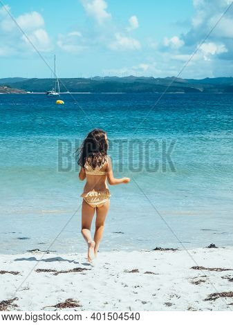 The Picture Shows A Vertical Shot Of The Back Of A Little Girl In A Bikini Running Along The Beach T