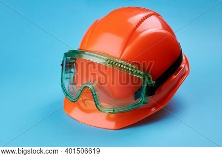 Orange Protective Helmet And Safety Glasses Near It On A Bright Blue Background. Protective Workwear