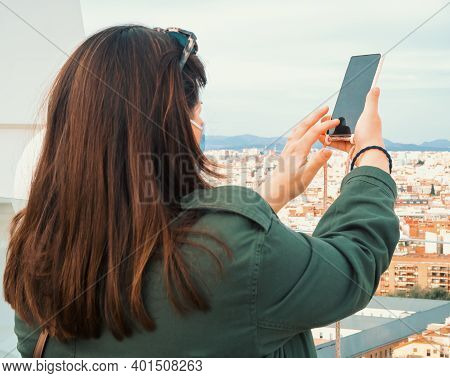 The Picture Shows Back View Of A Caucasian Woman With A Mask For Covid-19 Taking A Photo With Her Sm